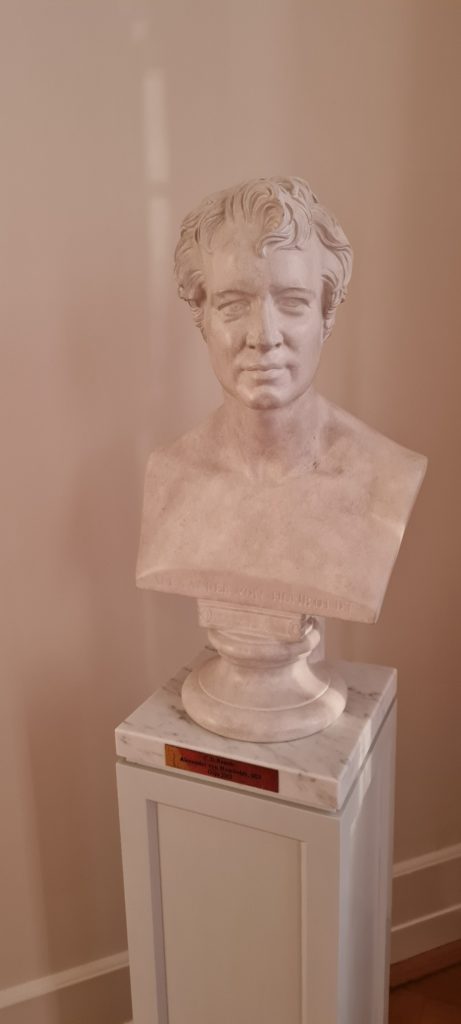 A photograph of Alexander von Humboldt's bust on a pedestal in front of a wall